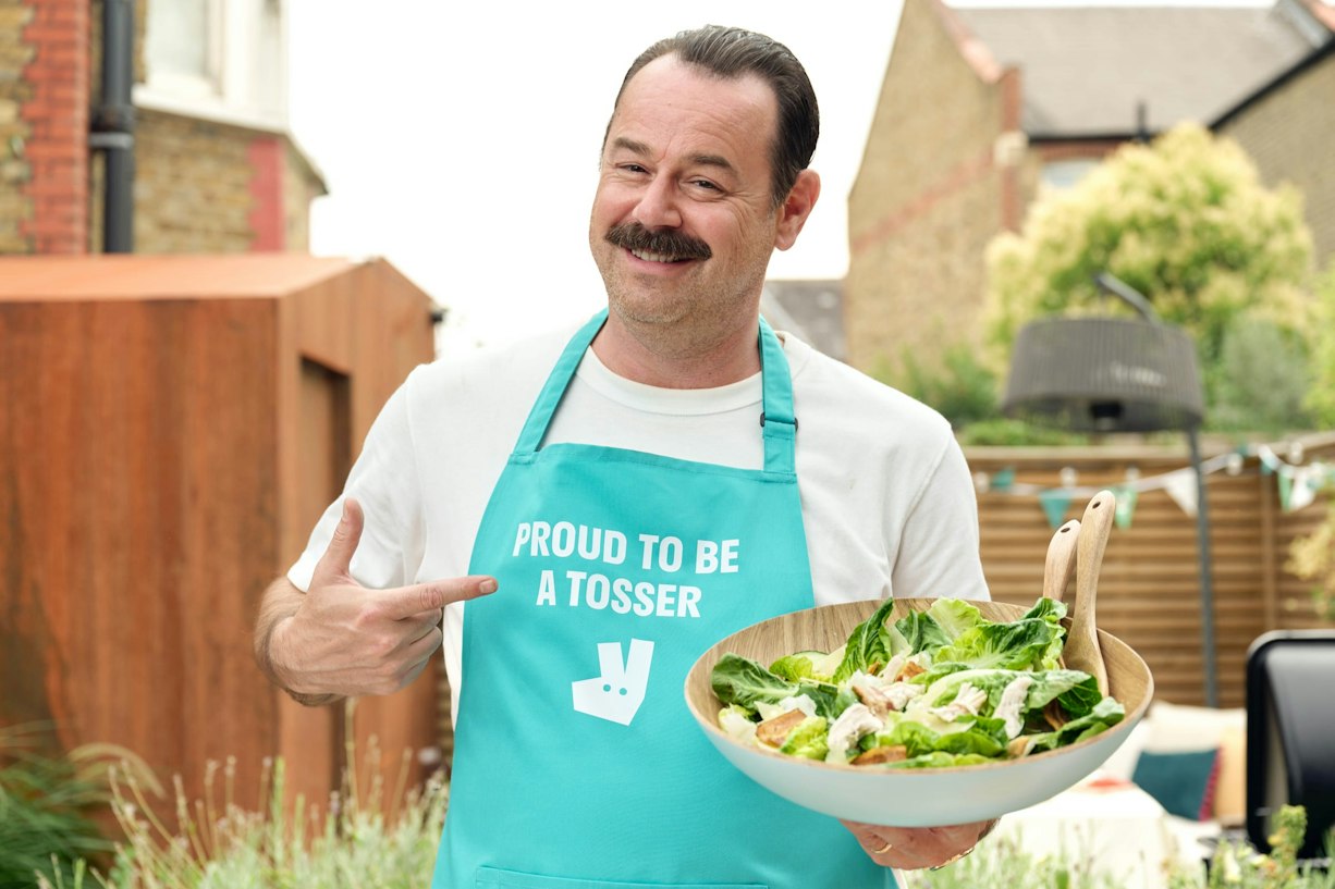 Danny Dyer pointing at his Proud To Be A Tosser apron for Deliveroo