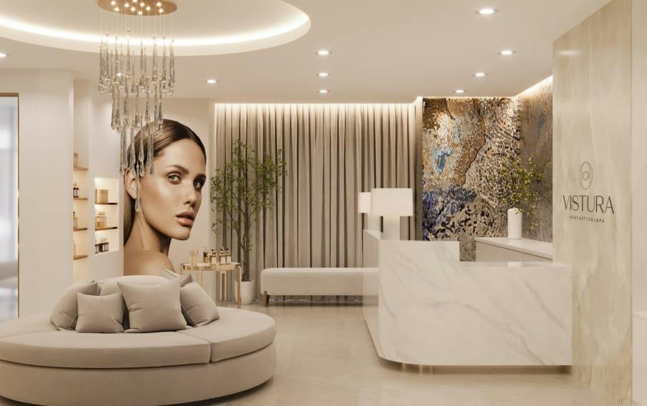 Elegant Vistura Aesthetics + Spa reception with marble desk, round beige sofa, crystal chandelier, and large portrait