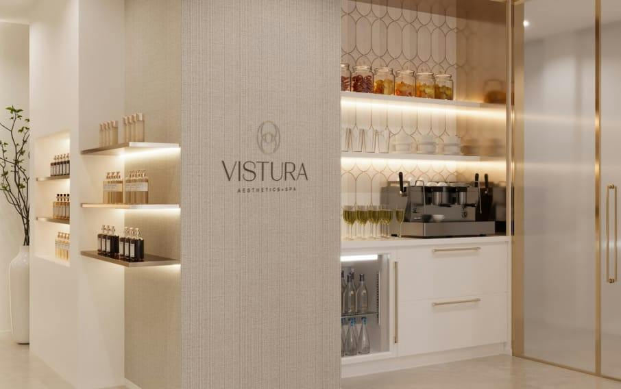 Vistura Aesthetics + Spa reception area with lit product shelves, espresso machine, champagne glasses, and beverage fridge