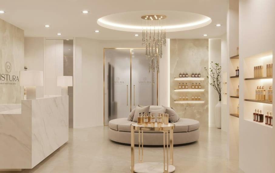 Elegant cream-and-gold spa reception with marble desk, crystal chandelier, round sofa, and product shelves, with