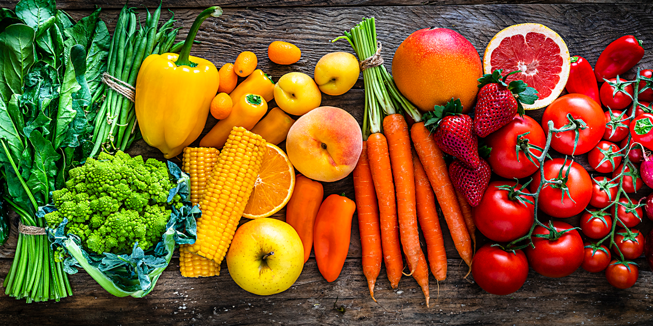 Top view of an assortment of colorful fruits and vegetables arranged side by side on a dark wooden table.