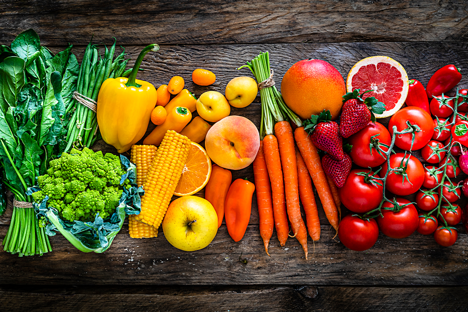 Top view of an assortment of colorful fruits and vegetables arranged side by side on a dark wooden table.