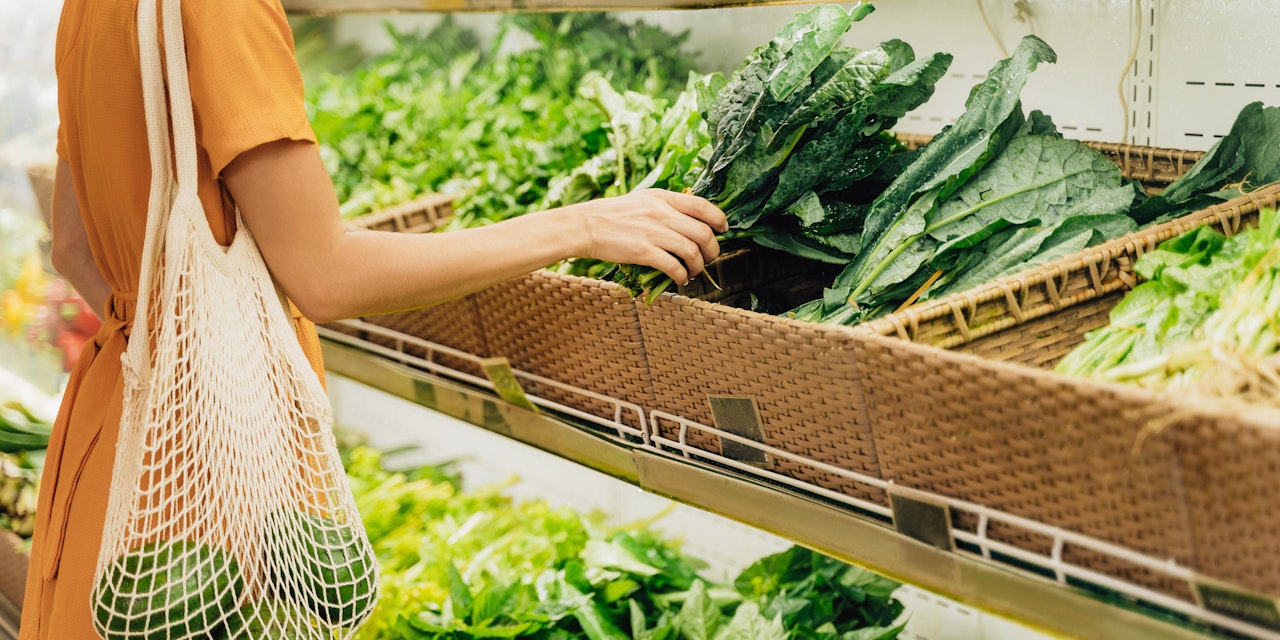 Woman buying vegetables Woman with mesh shopping bag buying vegetables at the grocery shop