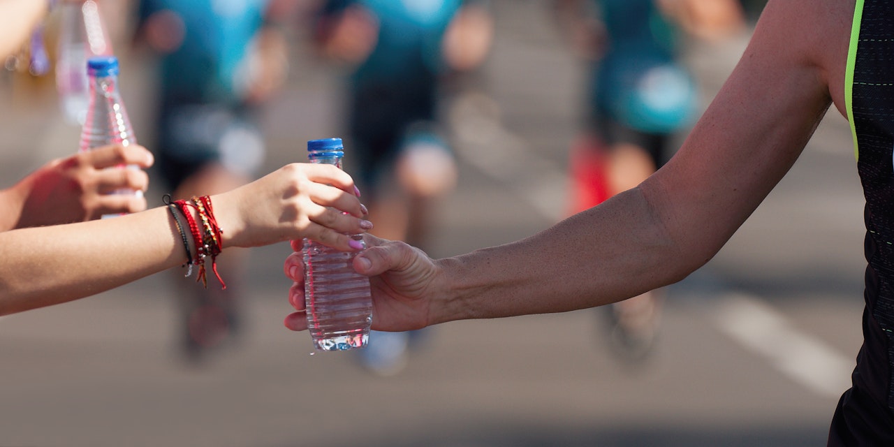 Person handing water bottle to a runner at a marathon water station