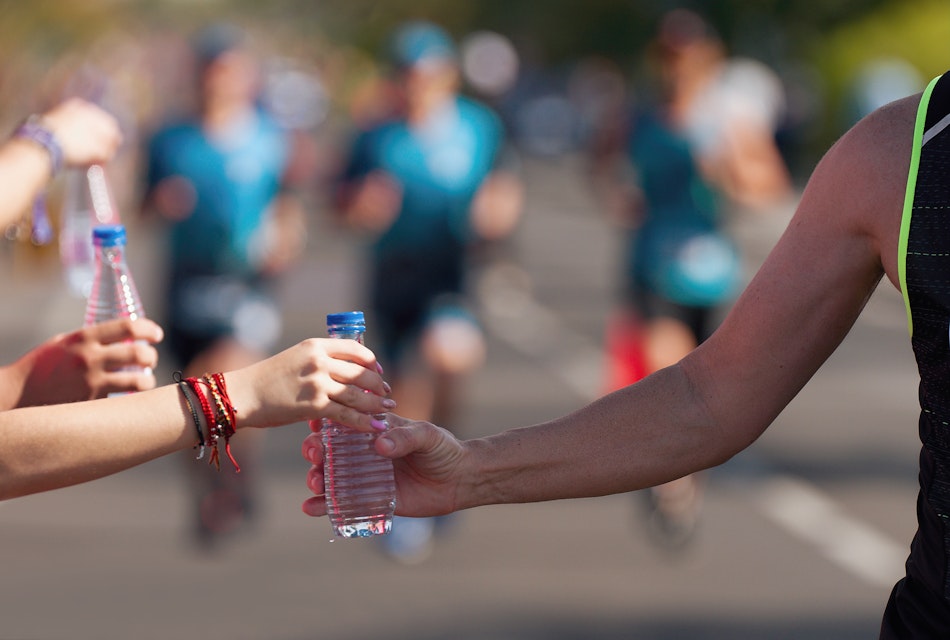 Person handing water bottle to a runner at a marathon water station