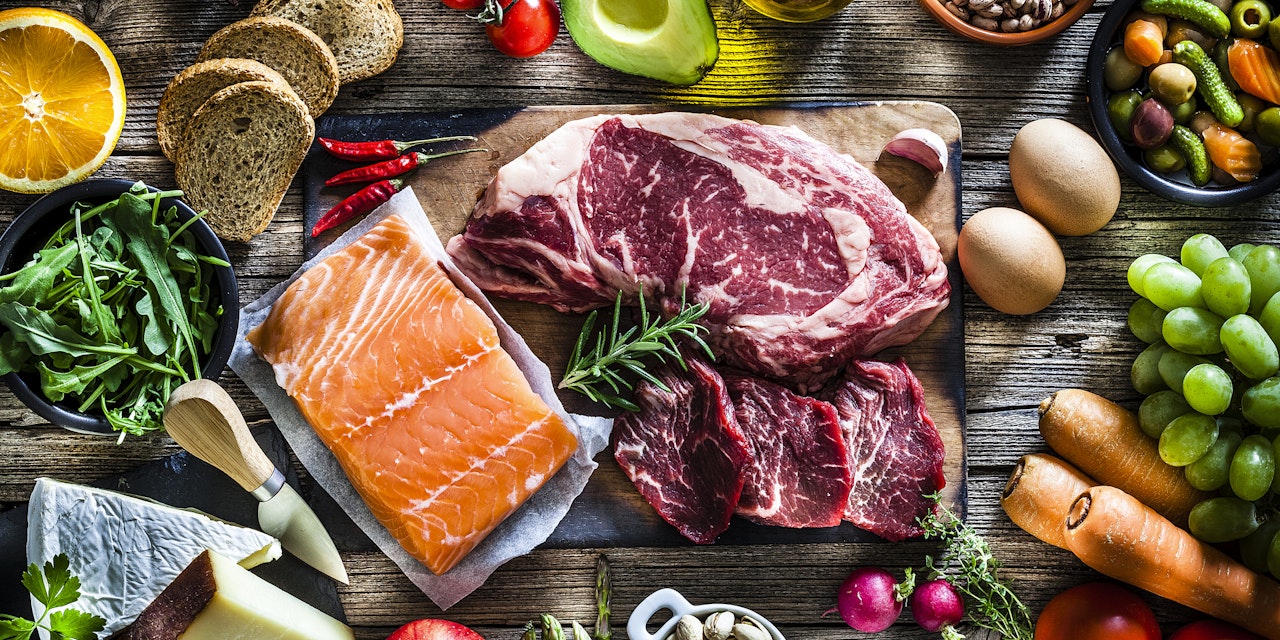Table filled with a great variety of food types, like steak, salmon, fruits and vegetables