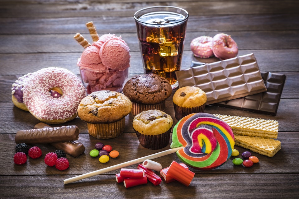 Assortment of sugary foods like candies, gummy candies, donuts, soda, chocolate, lollipop, wafers and cupcakes.