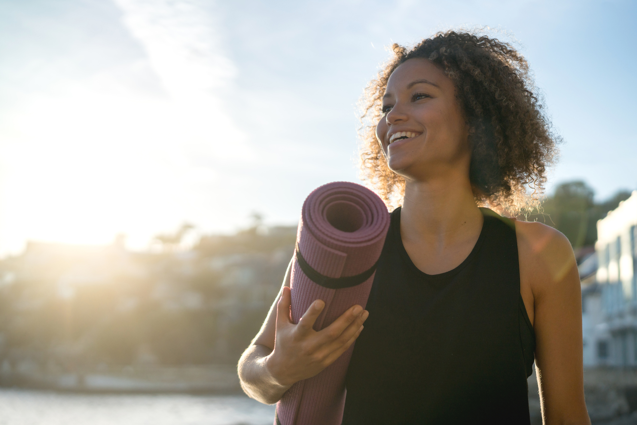 Happy woman holding a yoga mat at the beach 