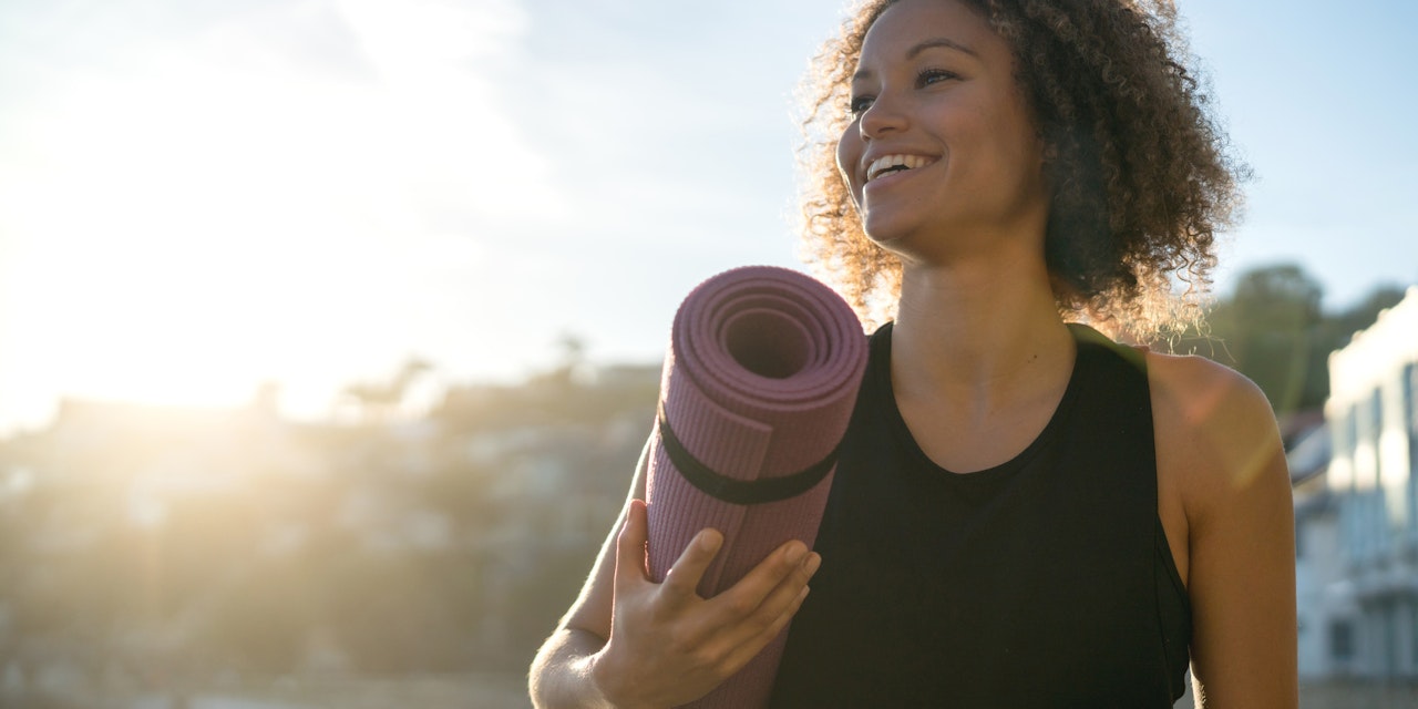Happy woman holding a yoga mat at the beach 