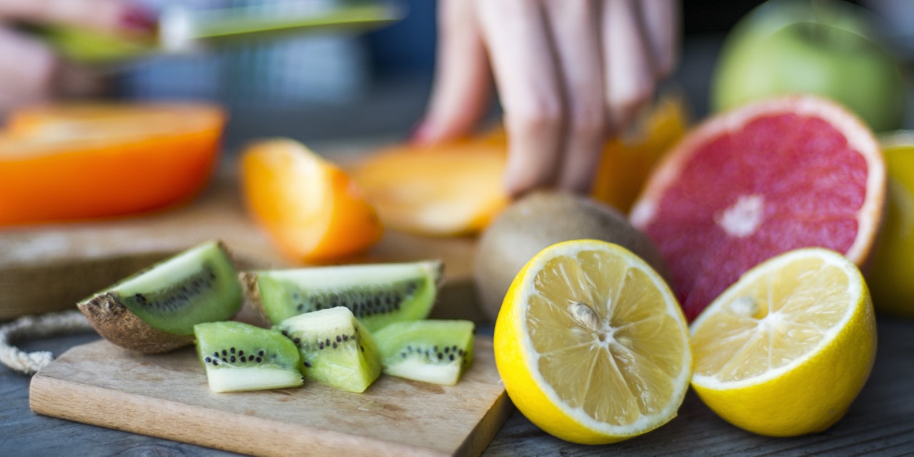Person cutting fruits like persimoon, kiwi and lemon.