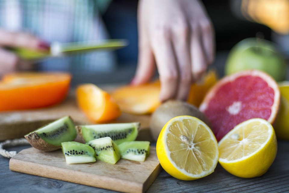 Person cutting fruits like persimoon, kiwi and lemon.