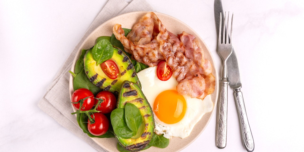Keto breakfast with grilled bacon and avocado, fried eggs, spinach and cherry tomatoes