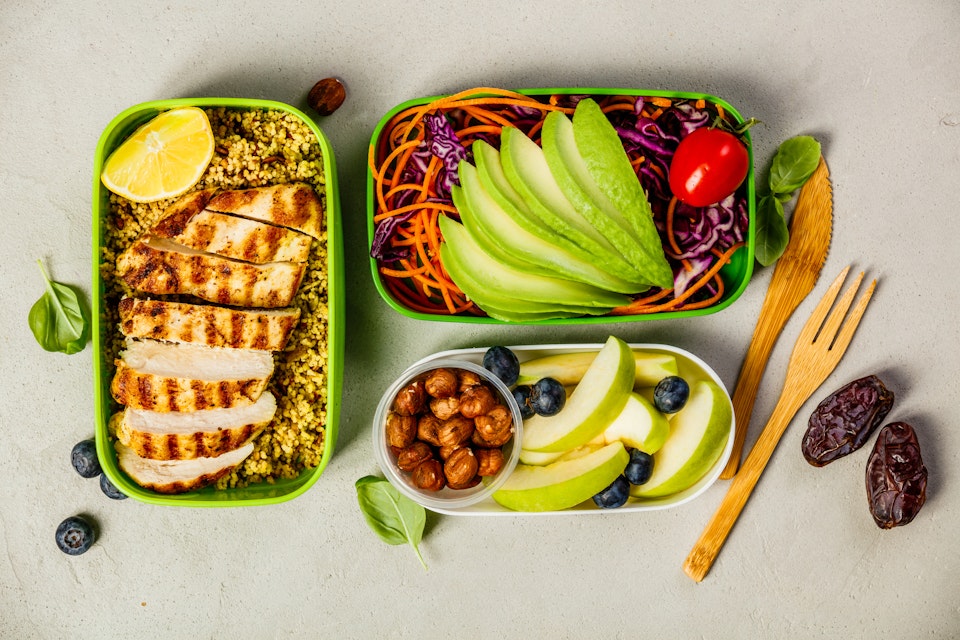 Healthy meal prep containers with couscous, grilled chicken breast, salad, avocado and fruits.