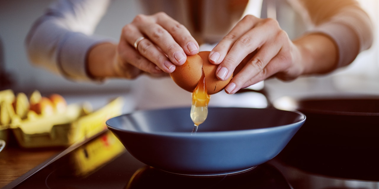 A picture of a lady's hands breaking an egg into a blure bowl on her countertop