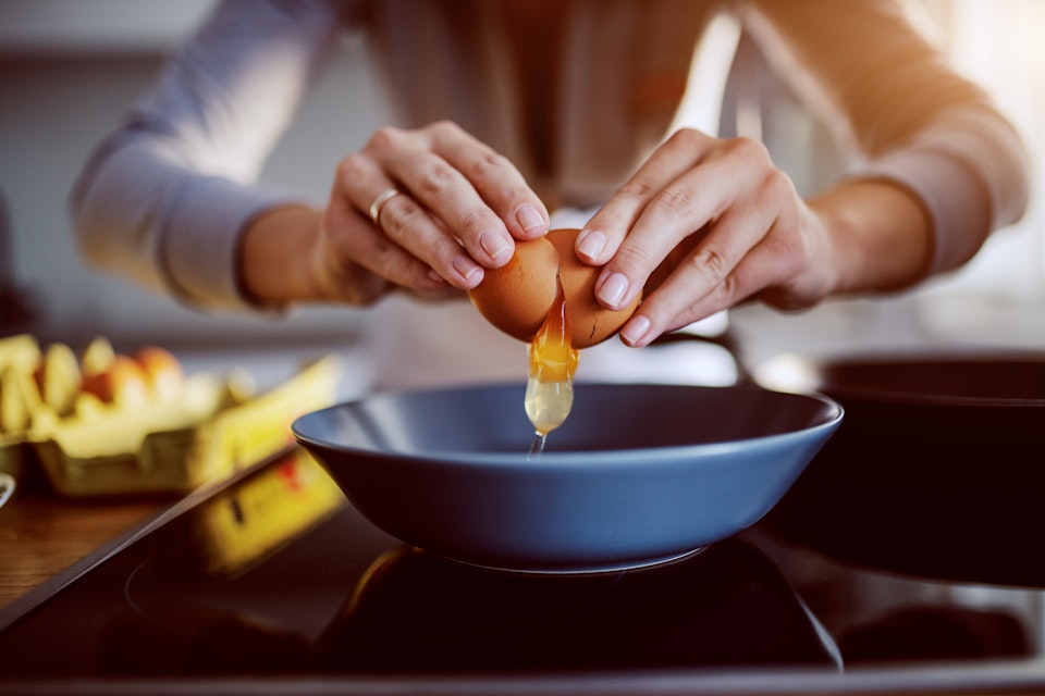 A picture of a lady's hands breaking an egg into a blure bowl on her countertop