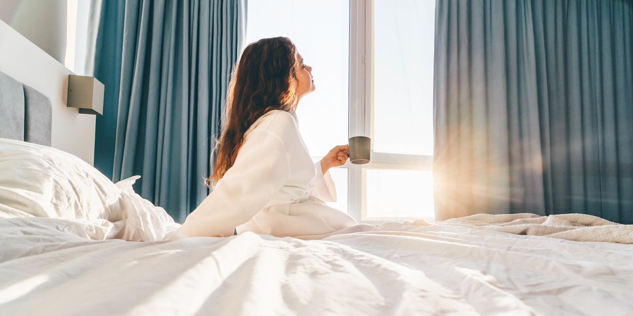 Young woman enjoying the morning with a cup of coffee in bed