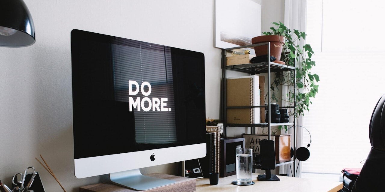 A home office monitor with the wallpaper that says "Do More."