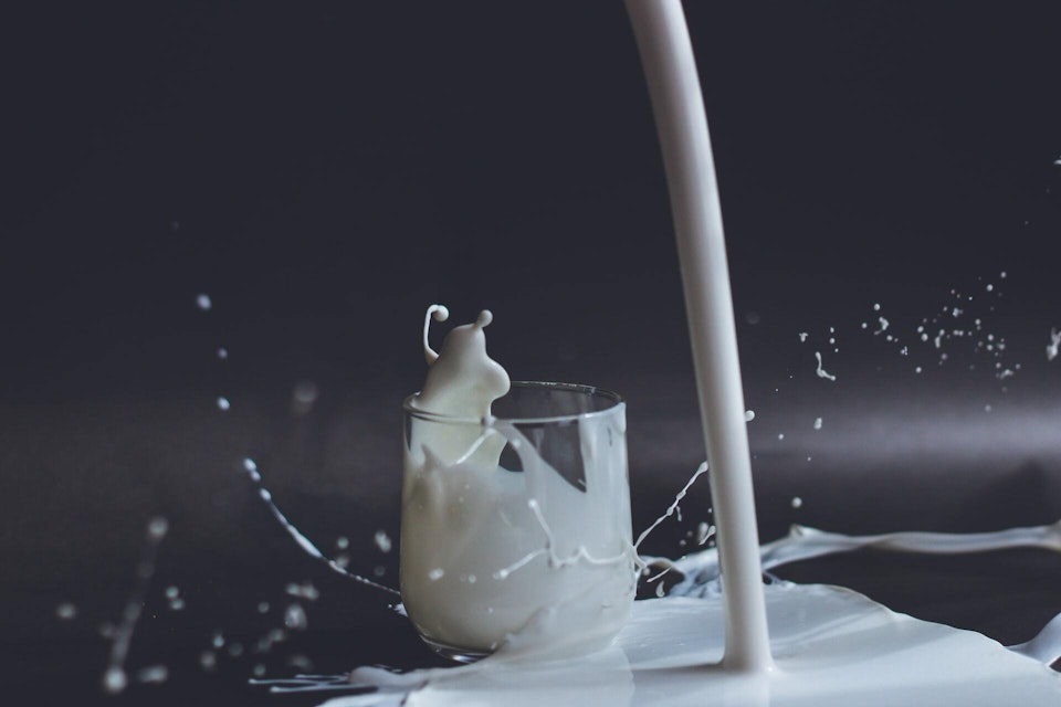 A glass of milk being poured and spilled