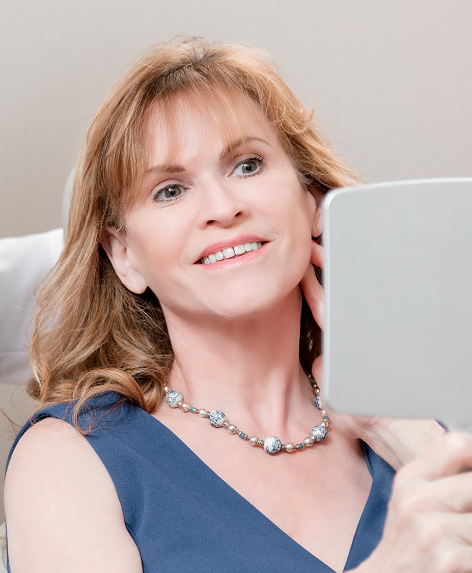 Smiling woman who is touching her neck while looking in a mirror.