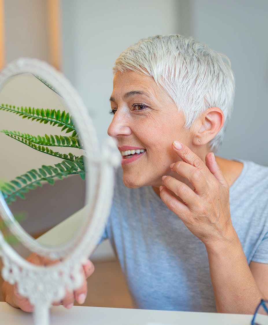 Older woman touching her face smiling looking in the mirror