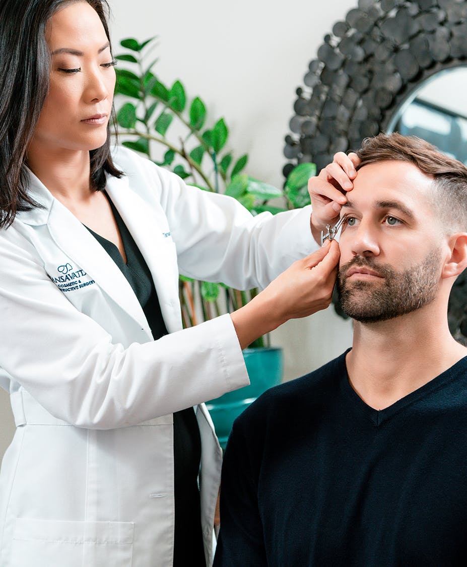 Dr. Tansavatdi measuring a young man's eyebrow