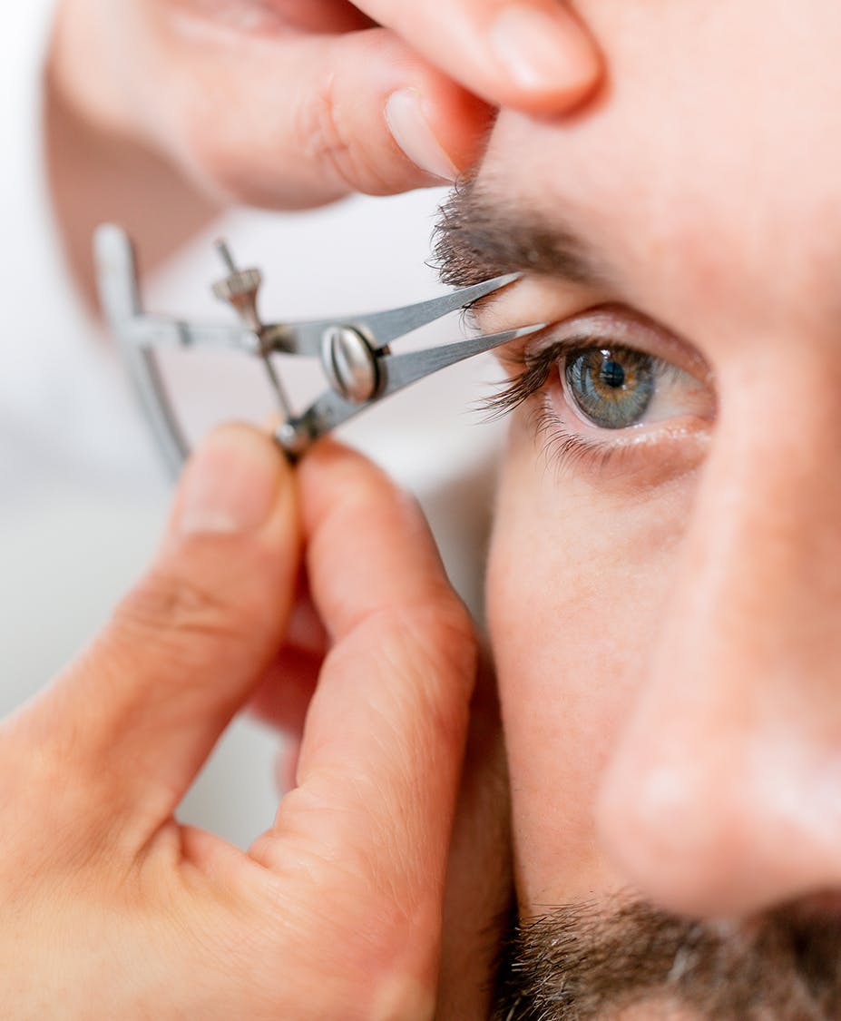 Hands measuring skin under man's eyebrow
