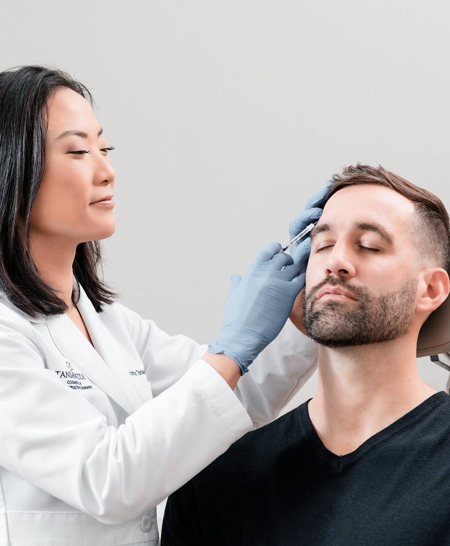 Dr. Tansavatdi applying an injection above a young man's eye brow