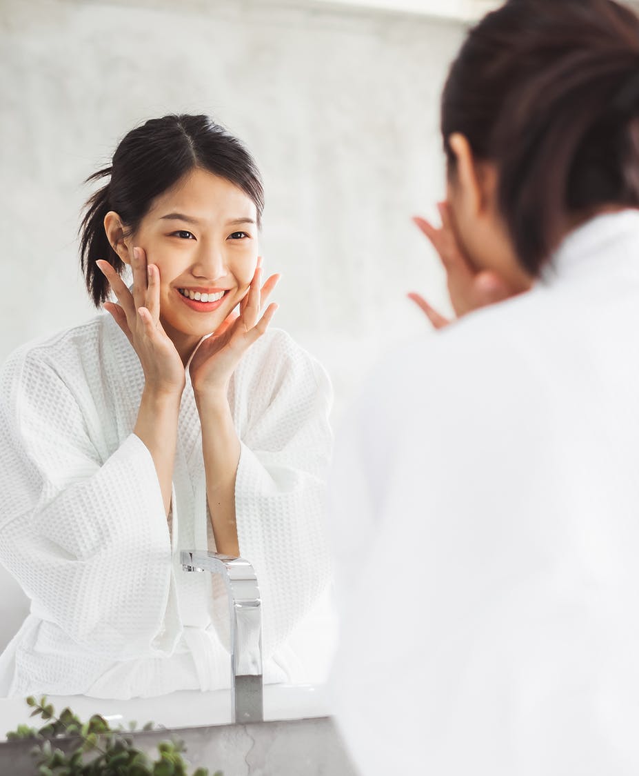 Young woman smiling looking in the mirror touching her face