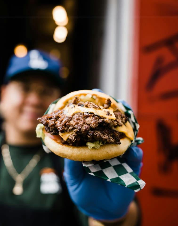 A staff member holds a double cheese smash burger out to the camera