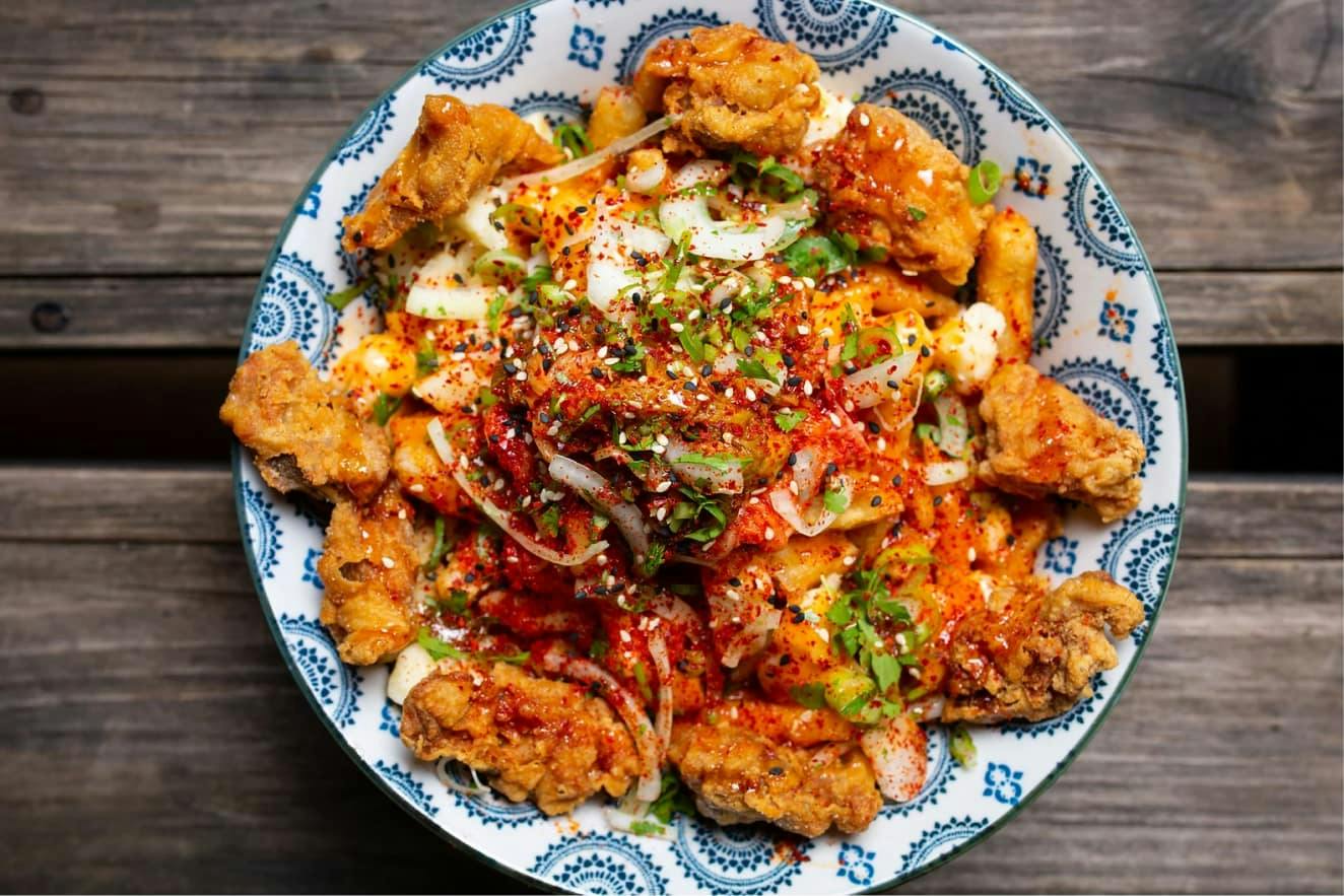 Poulet frit croustillant nappé de sauce épicée, oignon vert et sésame, dans un bol bleu et blanc