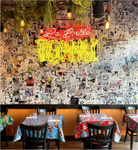 La salle à manger : mur de bandes dessinées, néon La Belle Tonki et tables aux nappes fleuries