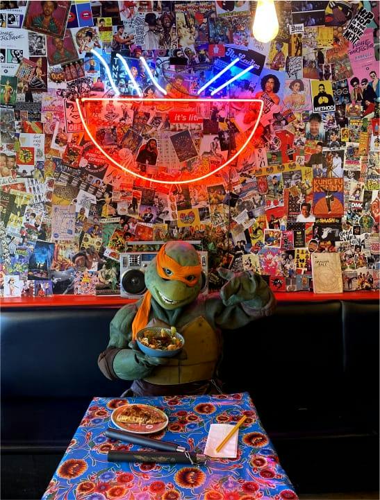 Une figurine de tortue ninja attablée sous le néon du restaurant