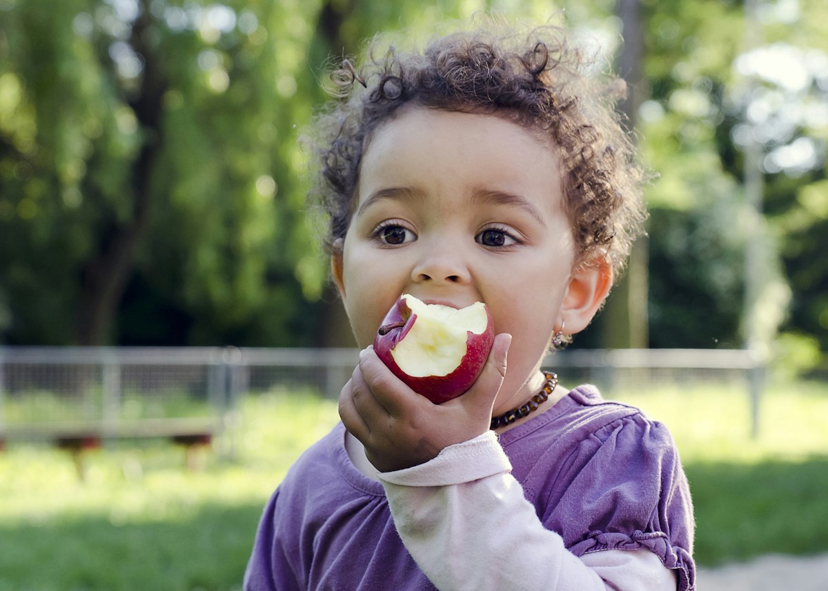 Child,Girl,Eating,An,Apple,In,A,Park,In,Nature.