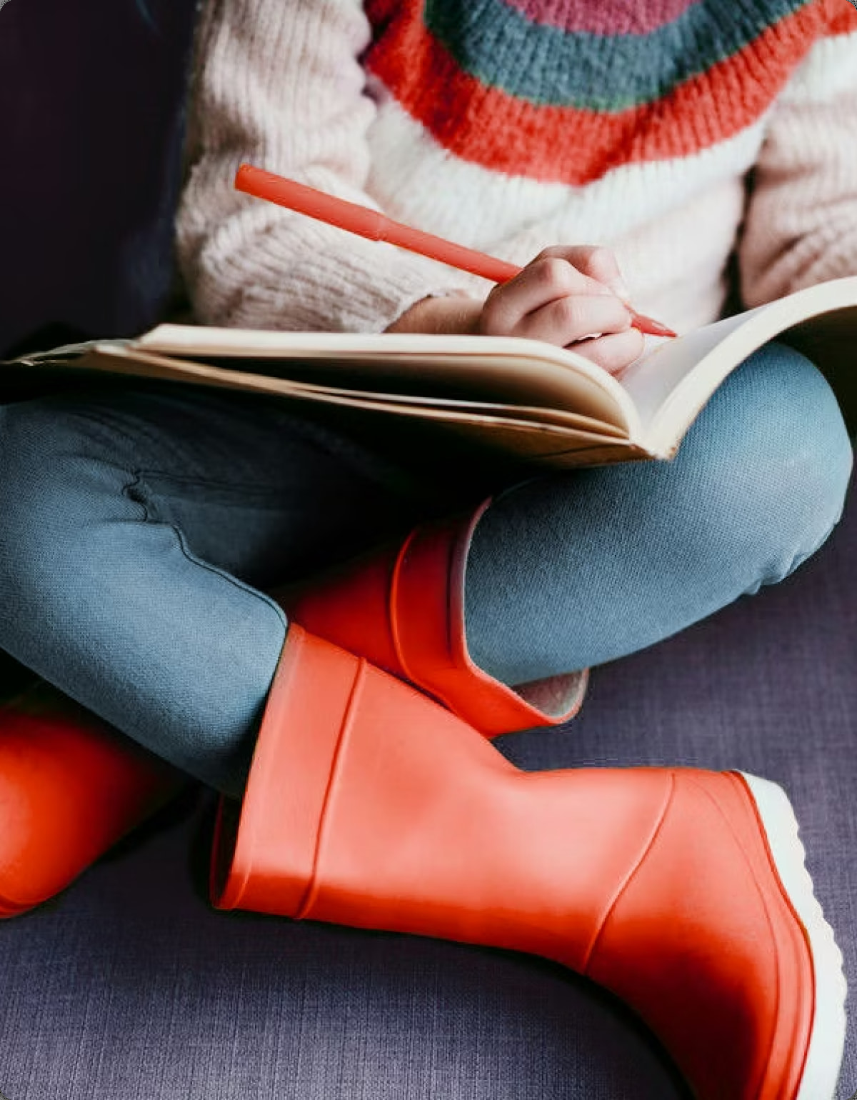 Child in red rain boots reading in an armchair