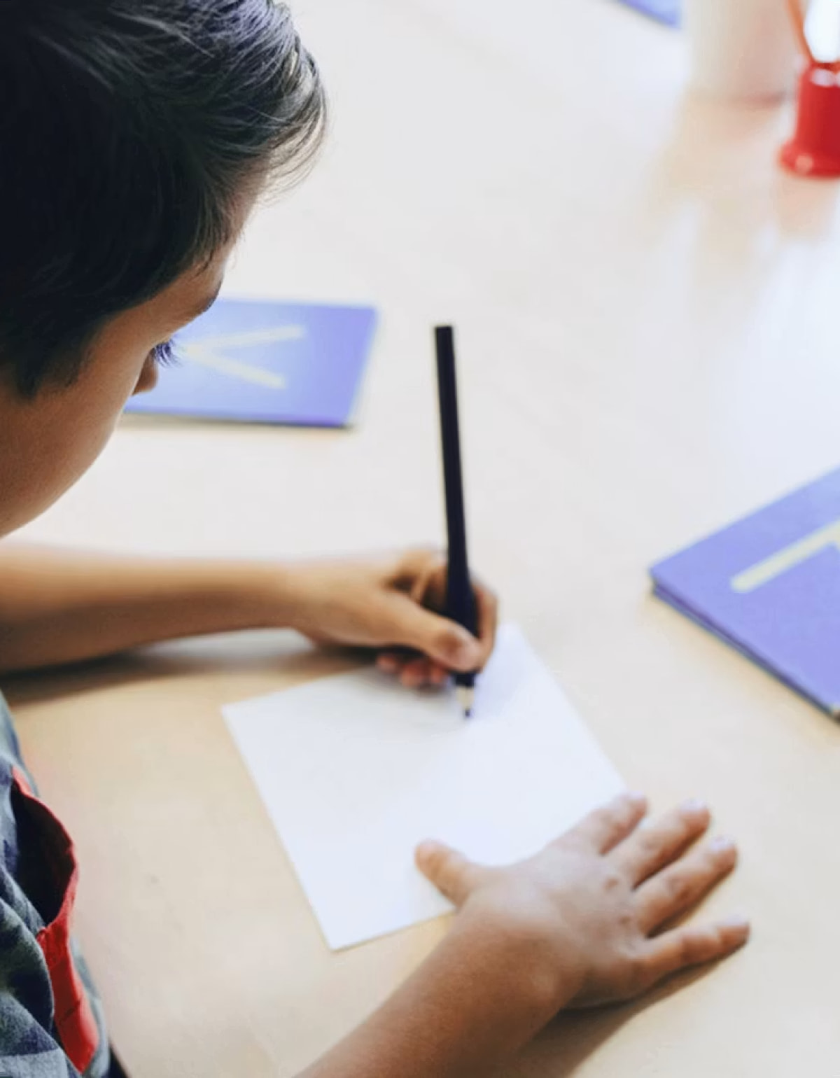 Child writing on a card at a table, seen from above
