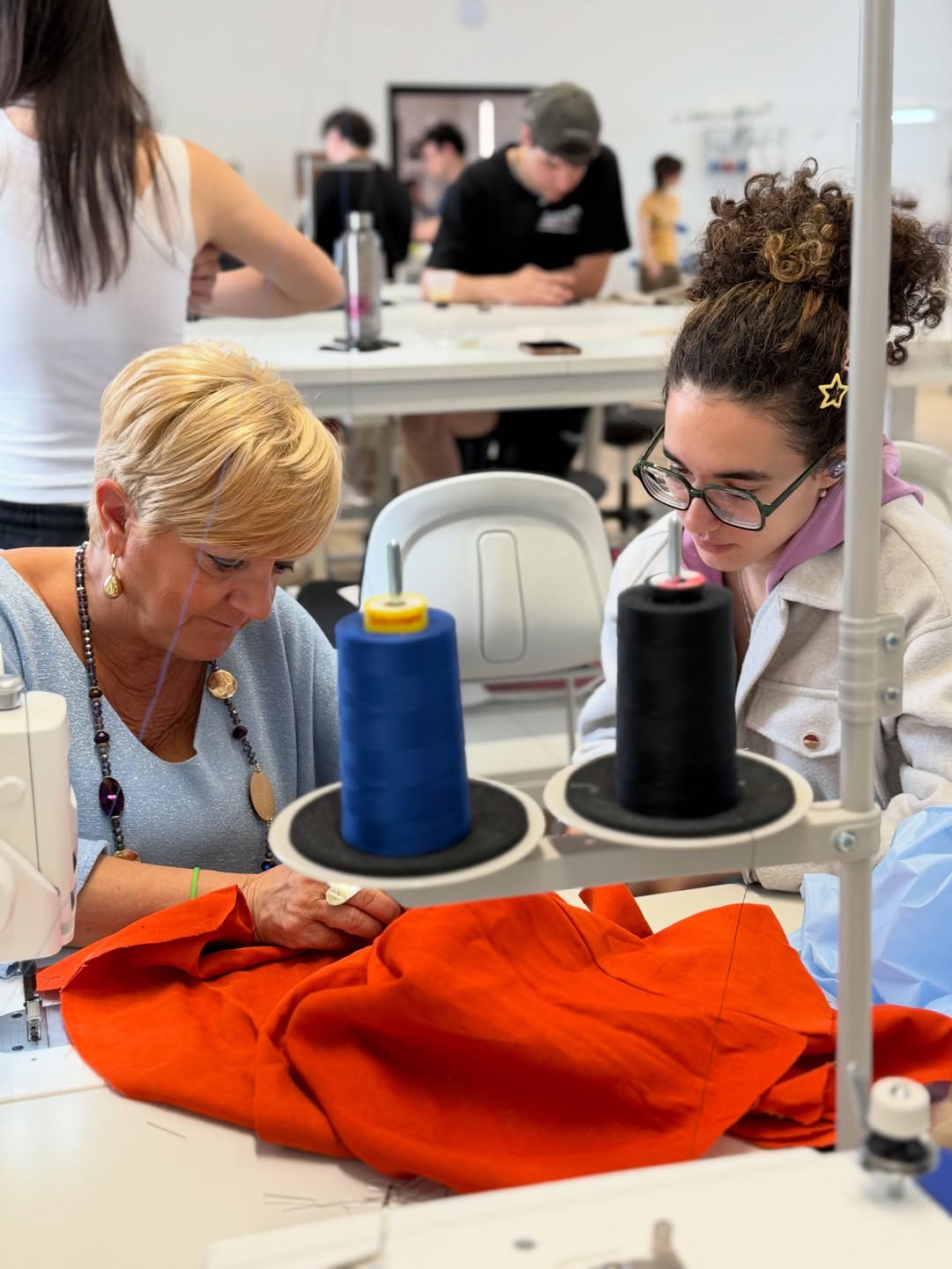 Docente e studentessa al lavoro su tessuti e macchine da cucire