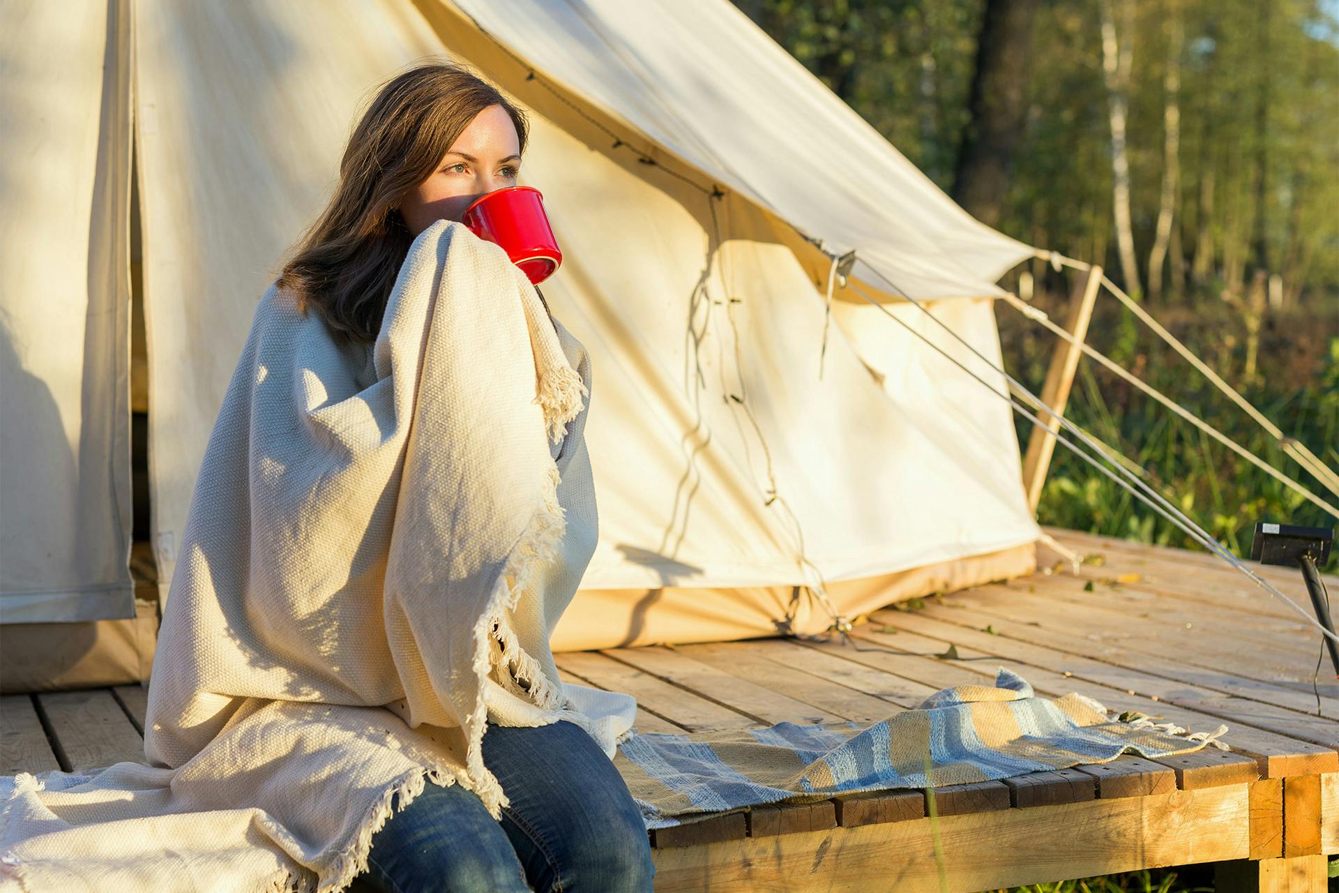 Nainen juo aamukahvia retkeilyteltan ulkopuolella metsässä