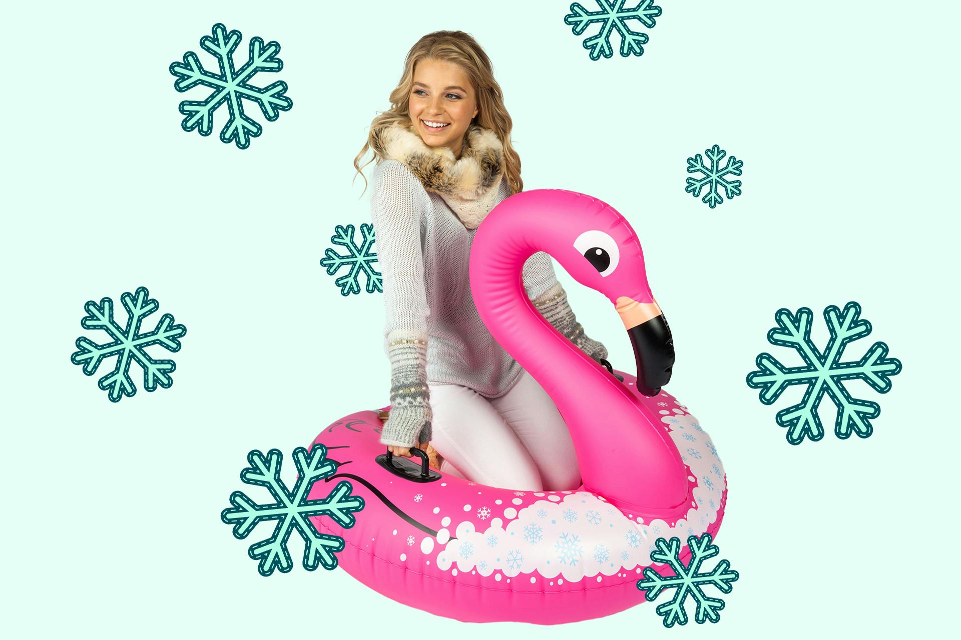 Glückliches Mädchen mit Flamingoschlitten im Schnee