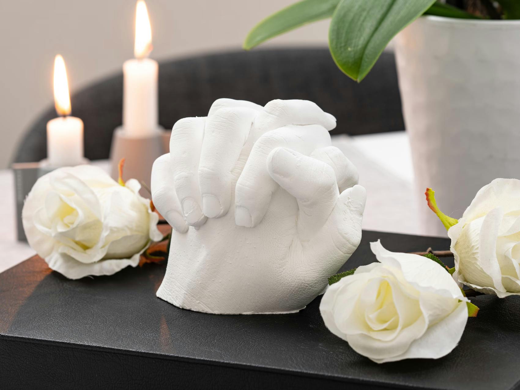 Nærbilde av en detaljert 3D-skulptur i gips som viser en voksen hånd som holder en babyhånd, en unik dåpsgave.