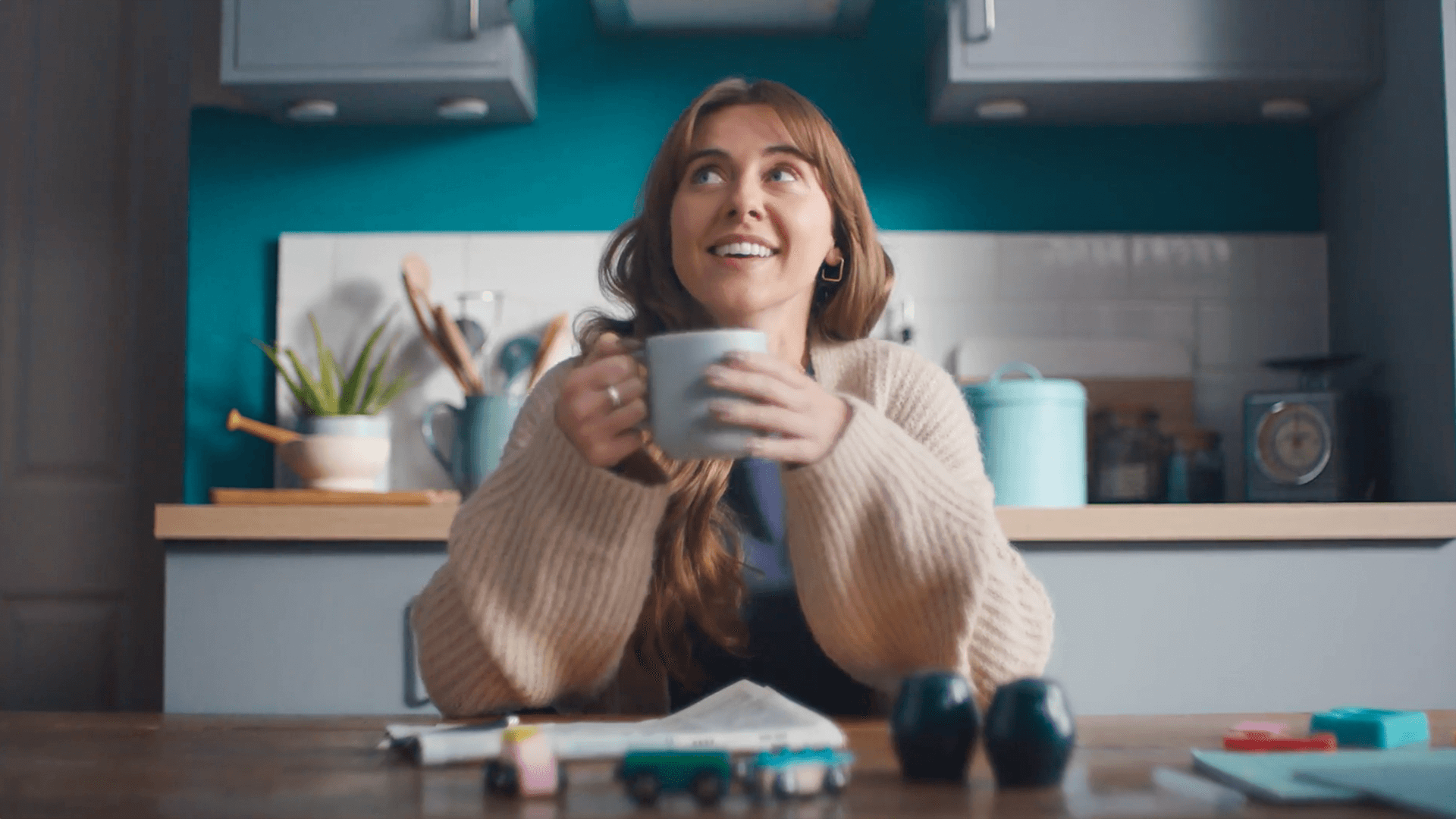 Woman sitting at a table smiling holding a mug