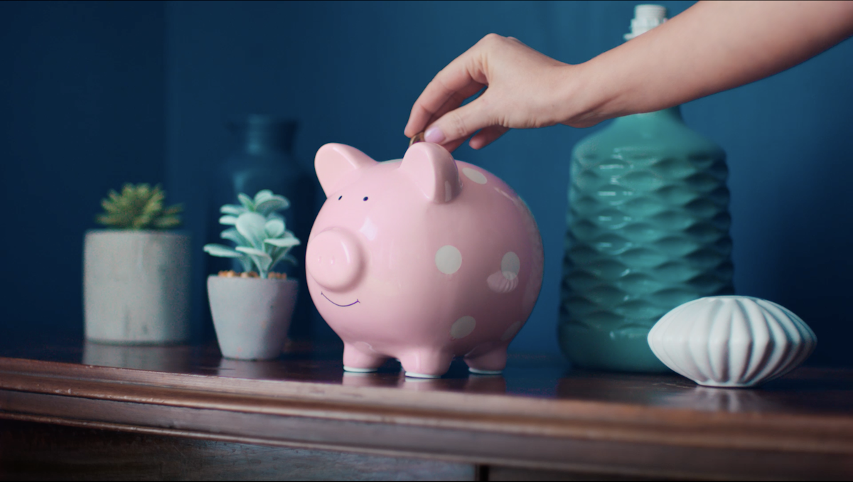 Somebody placing a coin in a Piggy Bank on a table