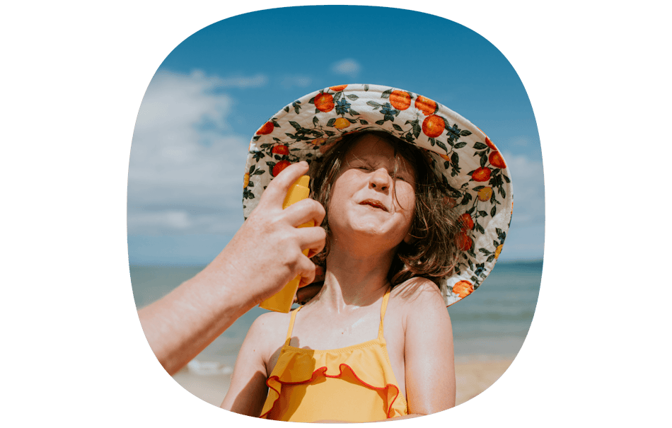 Girl on holiday in a hat being sprayed with sun screen