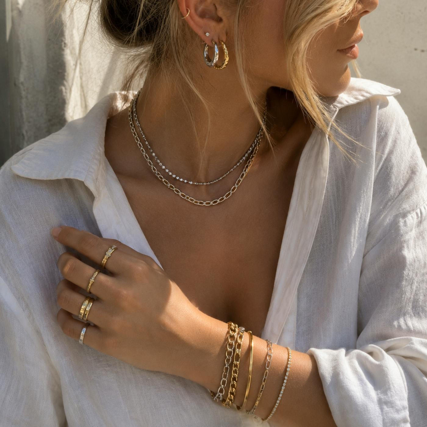 Can you mix gold and silver jewellery? Woman in a white shirt wearing layered silver and gold necklaces with stacked rings and bracelets