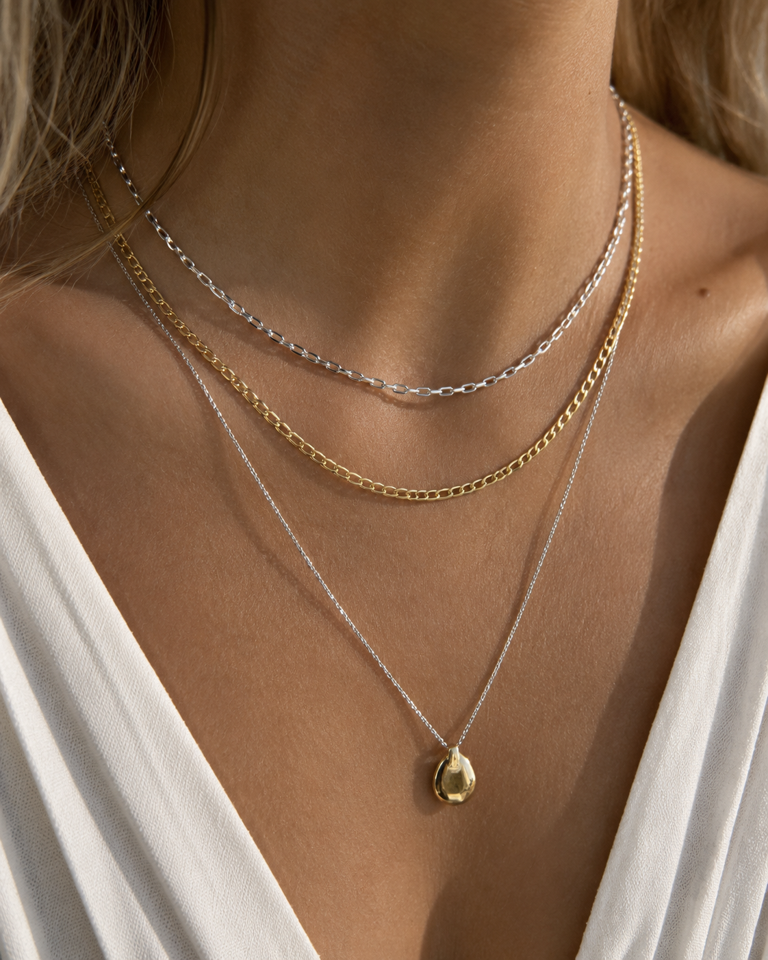 Close-up of layered silver and gold necklaces with a gold pendant