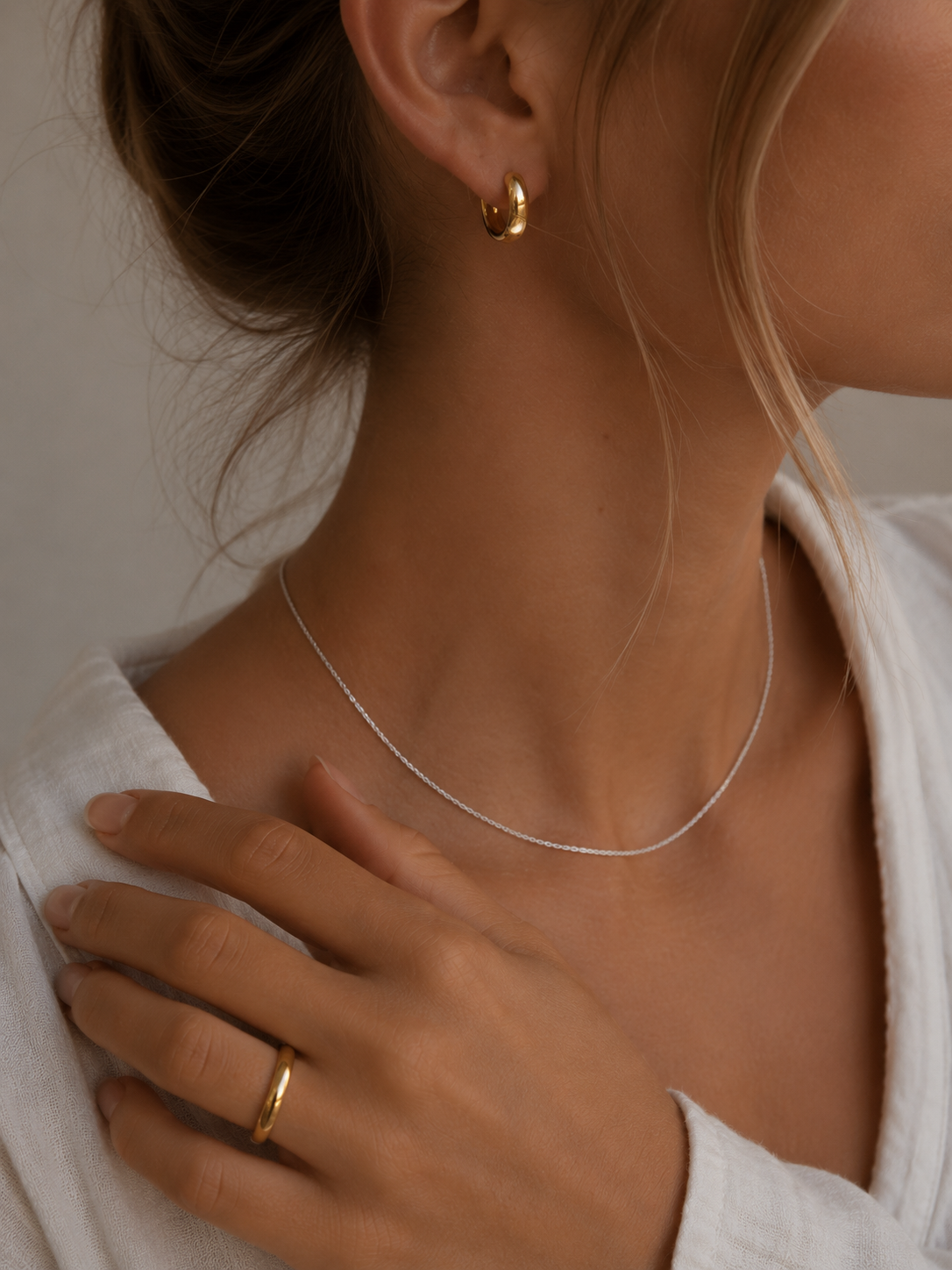 Gold hoop earring worn with a fine silver necklace and a gold ring