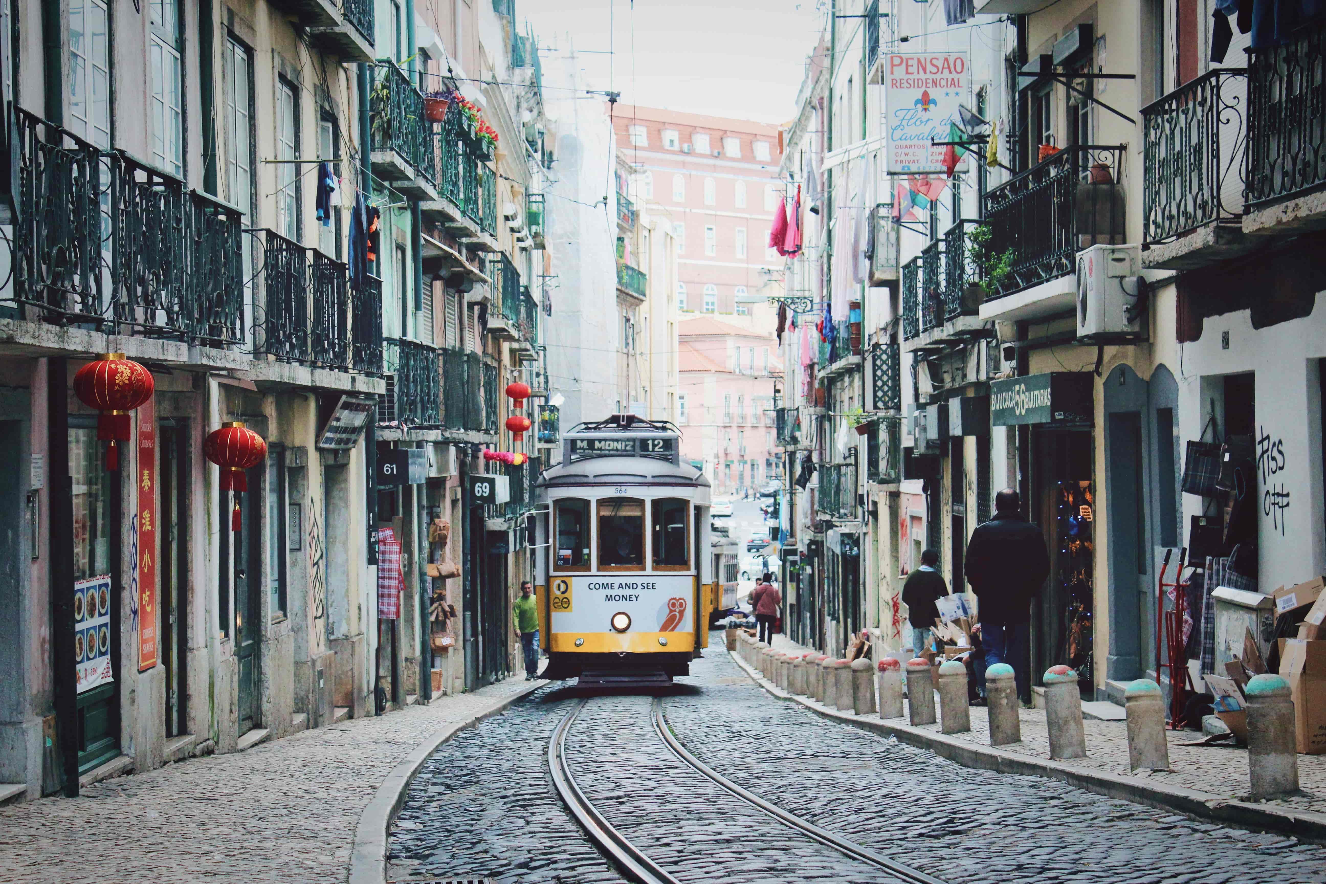 Gul spårvagn åker längs smal gata i Lissabon, en perfekt destination att flytta utomlands till 