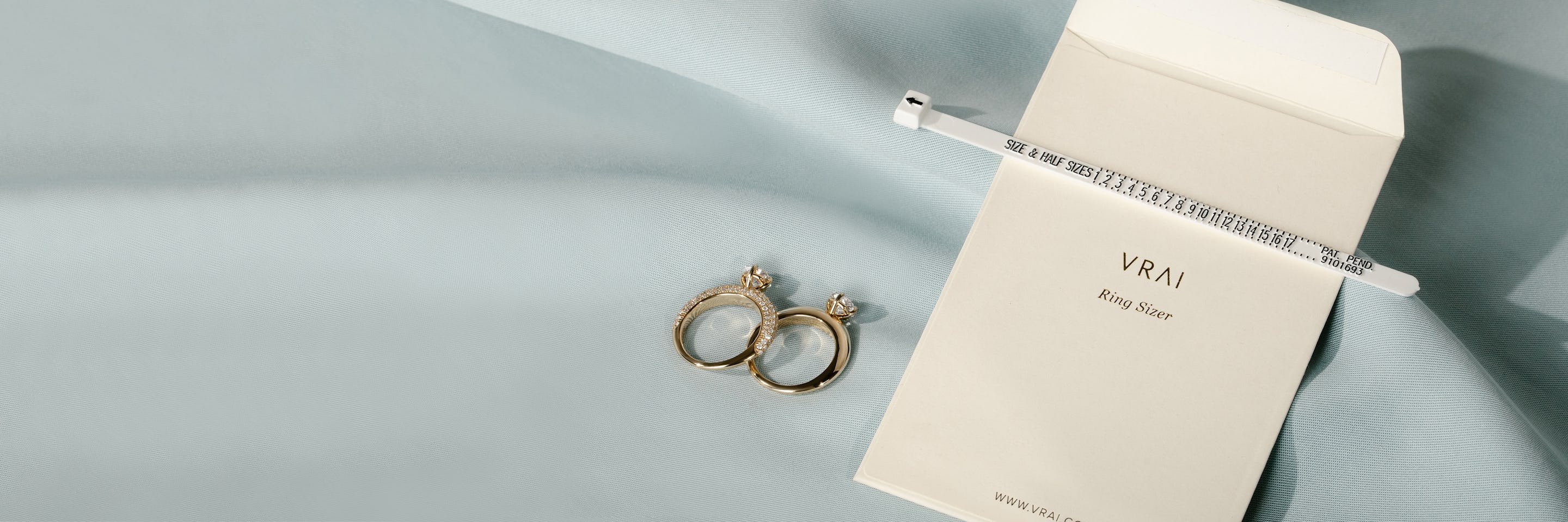 two engagement rings next to a ring sizer and package