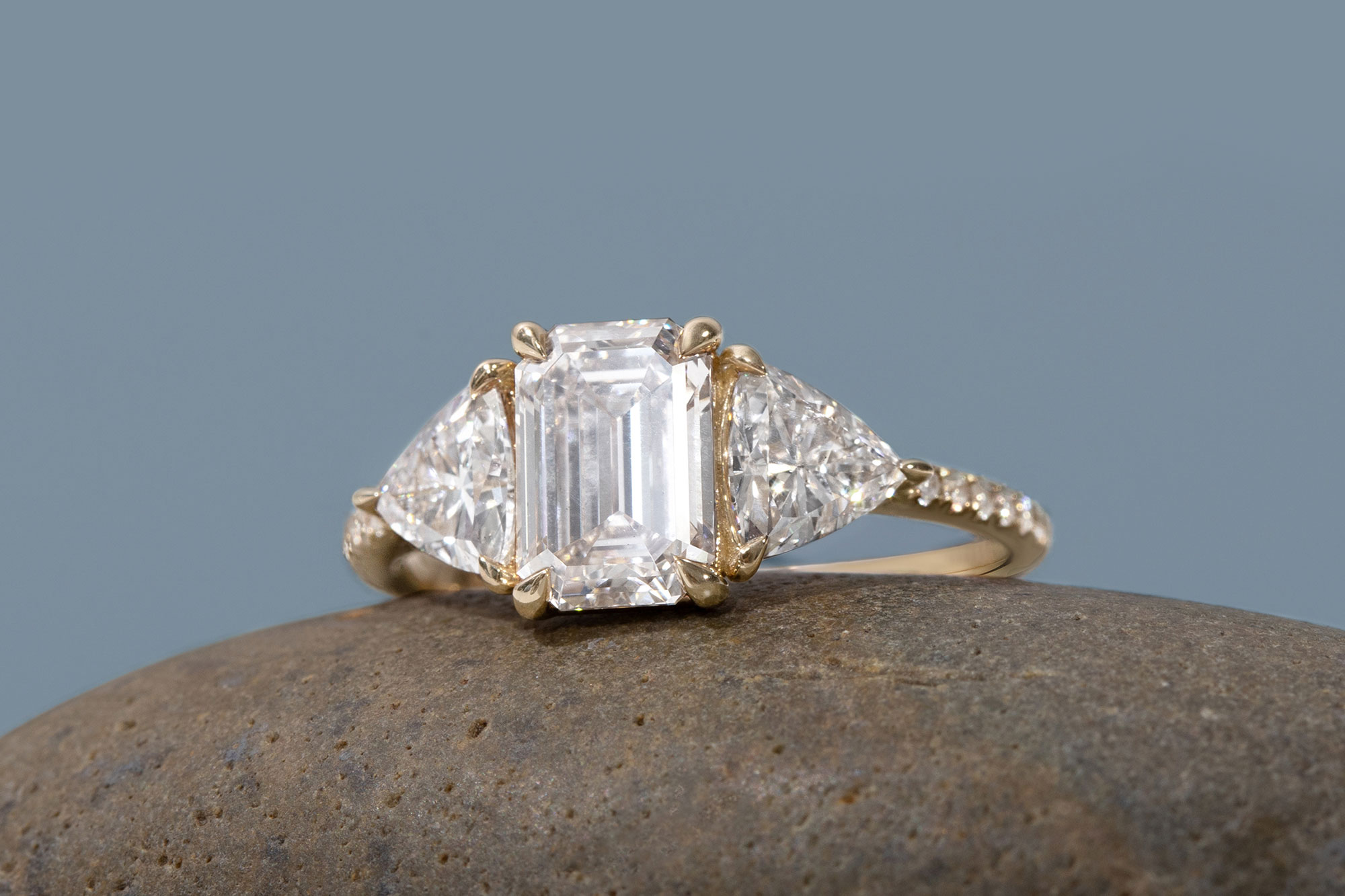 The emerald three stone engagement ring with trillion side stones and yellow gold pave band