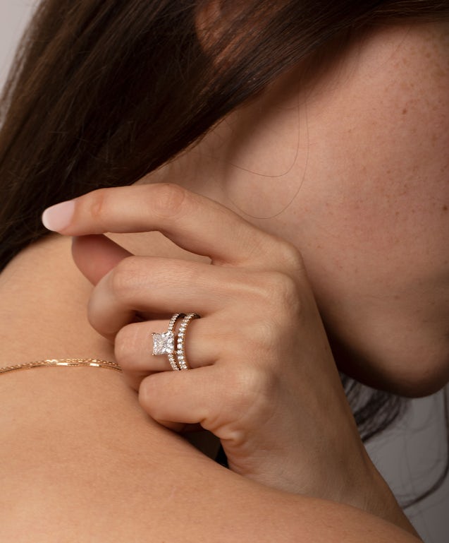 woman wearing a princess cut engagement ring with a matching wedding ring and holding her hand by her neck