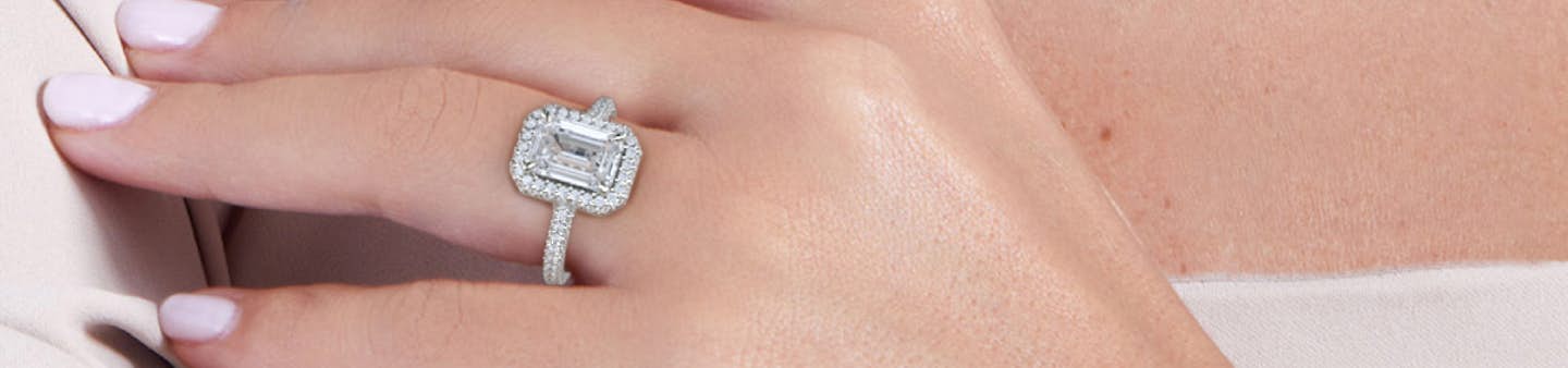 a hand with a VRAI created Emerald cut diamond Halo engagement ring in platinum